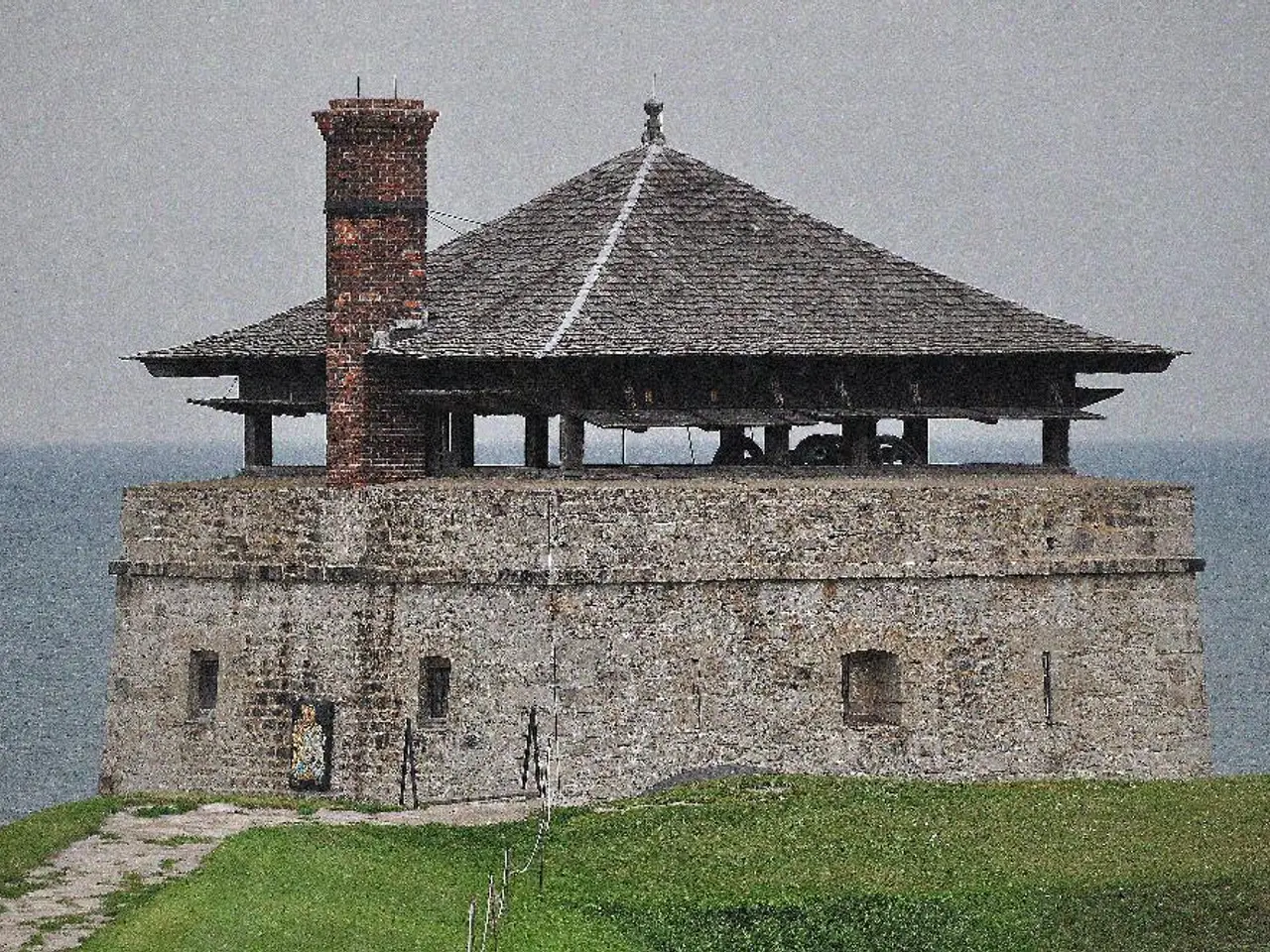 In this image there is a grassland, in the background there is a house and the sea.