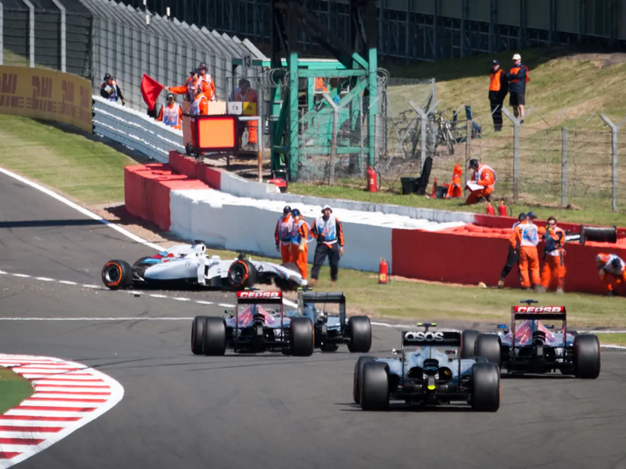 Vehicles are on the road. Here we can see people, fence, grass and hoarding.