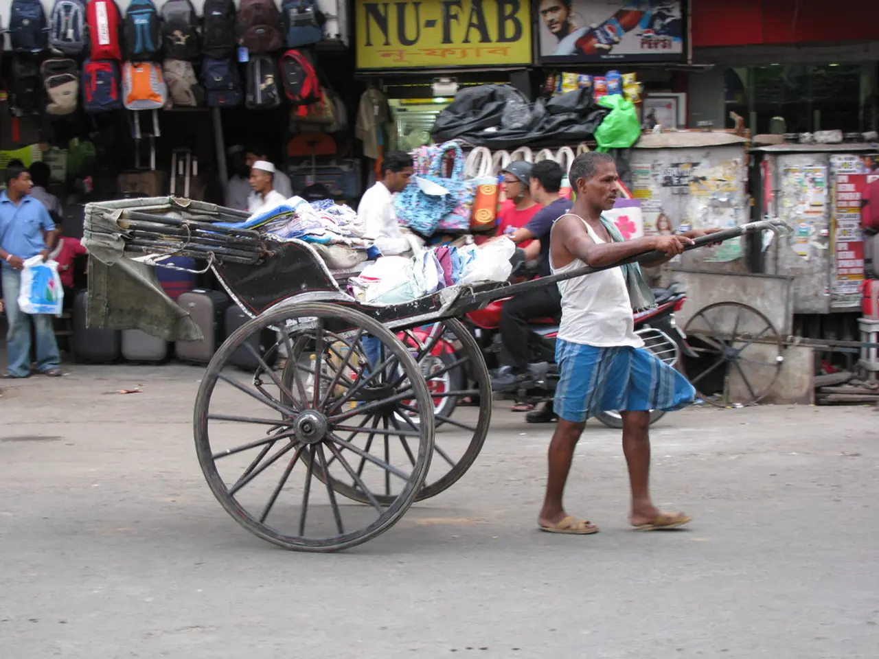 In this image, I can see a person standing on the road and holding pulled rickshaw. There are few...