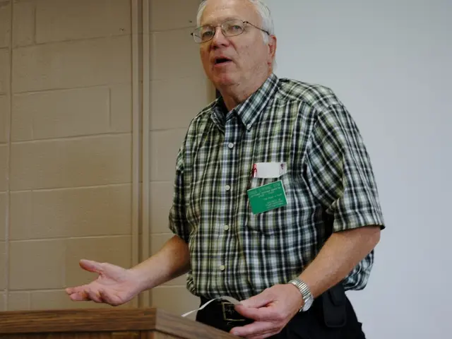 In this image in the center there is one person who is talking, and he is holding a paper and in...