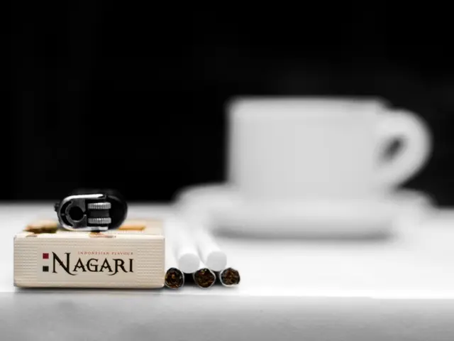 in this picture we can see a cup and saucer, cigarettes, and litter and box on the table.