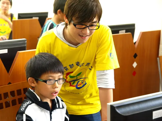 There is a man and a boy. Both are wearing specs. In front of them there is a computer. In the back...